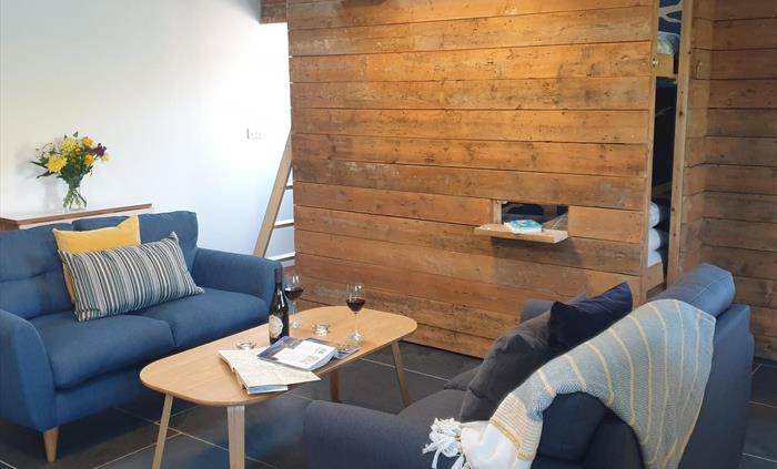 Sofas either side of a coffee table with a map and guide book open and a bottle of wine and 2 glasses.  Bunk beds in the background hidden behind a ti